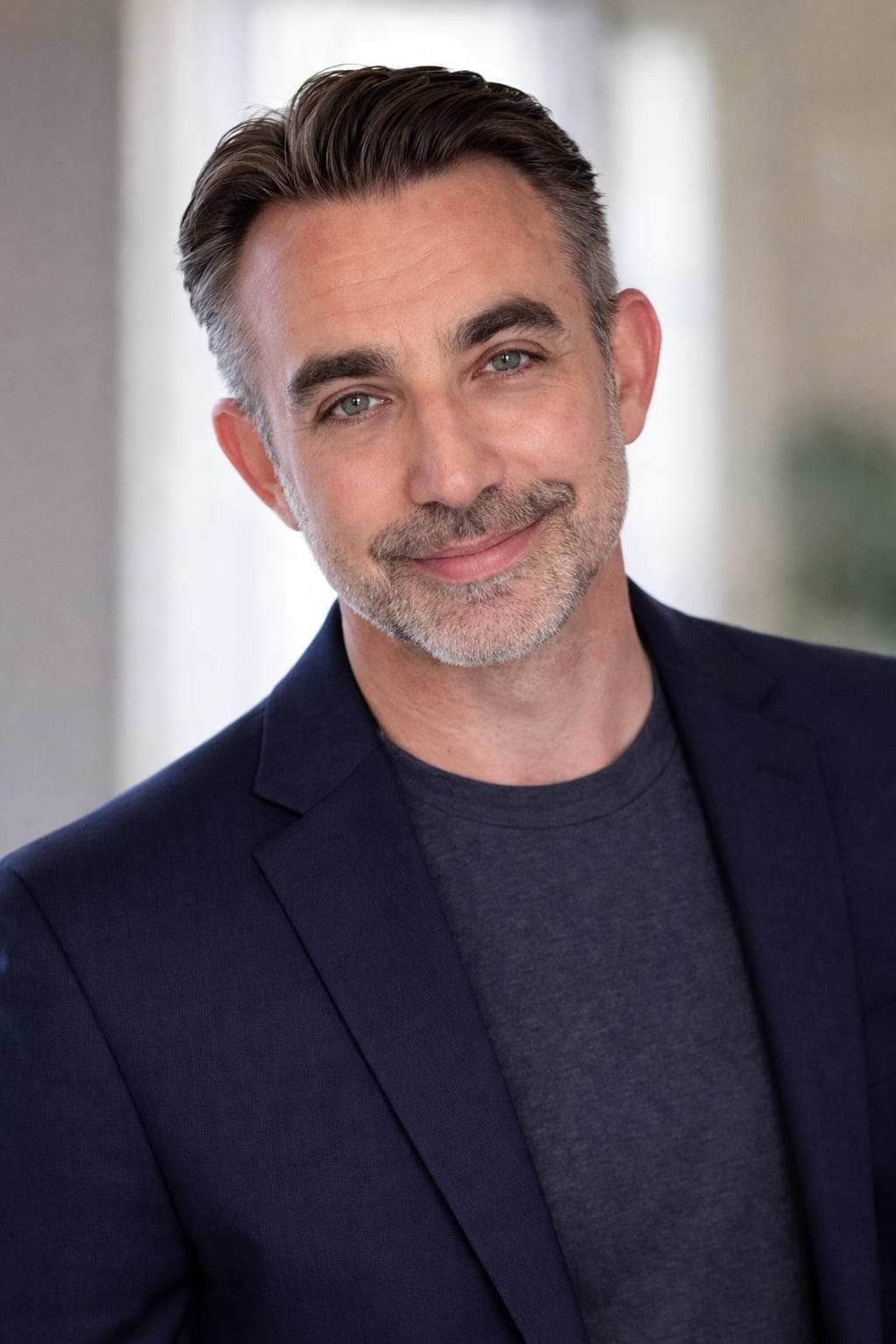 Smiling man with salt-and-pepper hair, beard, and green eyes, wearing a navy blazer.